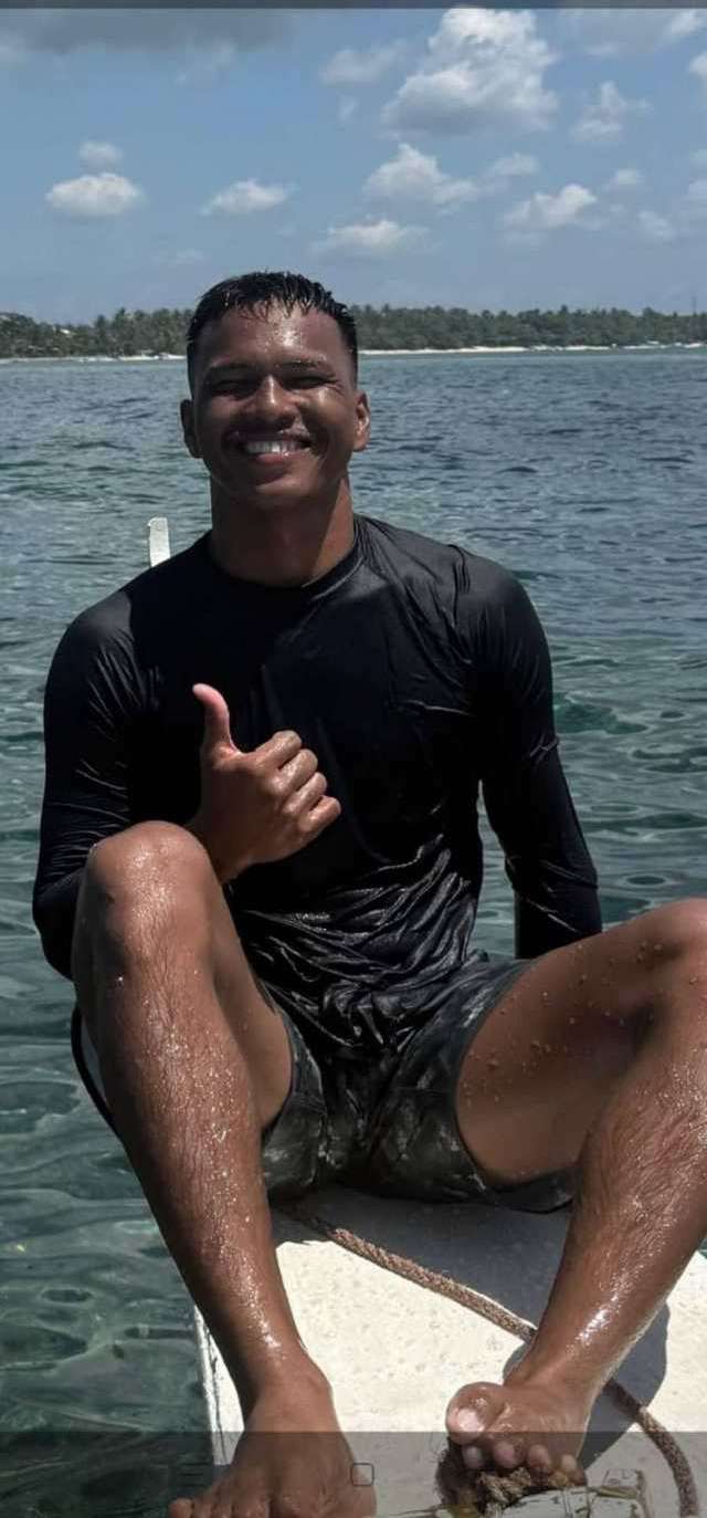 Un moniteur assis sur le balancier d'une bangka, la mer bleue derrière lui