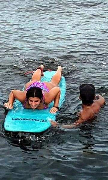 Un moniteur dans l'eau guide un élève allongé sur une planche bleu turquoise