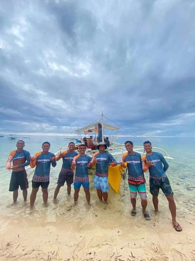 Un groupe de surfeurs locaux avec leurs planches, à côté d'une bangka sur la plage