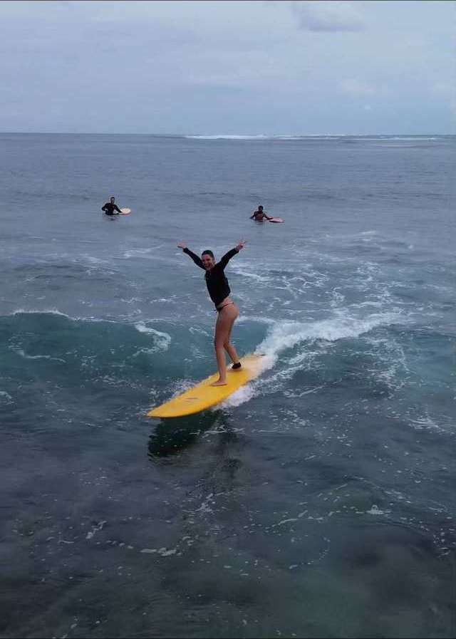 Une surfeuse debout sur sa planche, les bras écartés