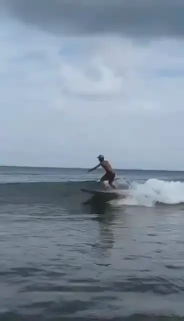 Un surfeur trace sur une vague par temps nuageux, les bras écartés