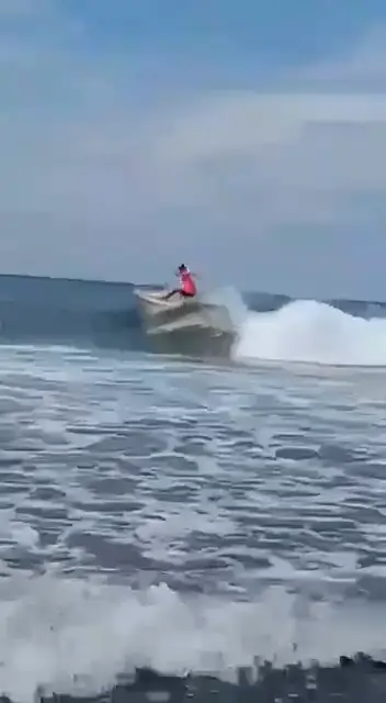 Un surfeur en lycra rose tourne sur une vague, l'eau gicle derrière lui
