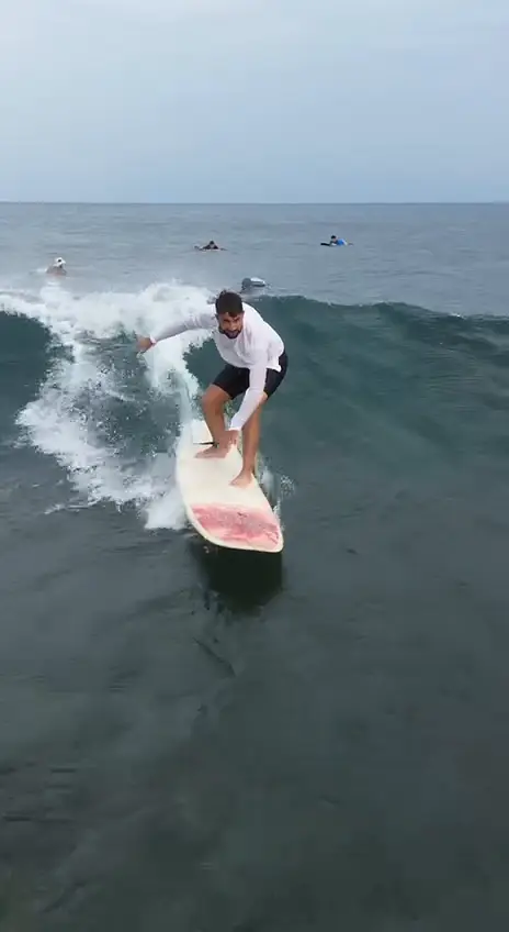 Un surfeur en lycra blanc sur une vague, filmé par drone